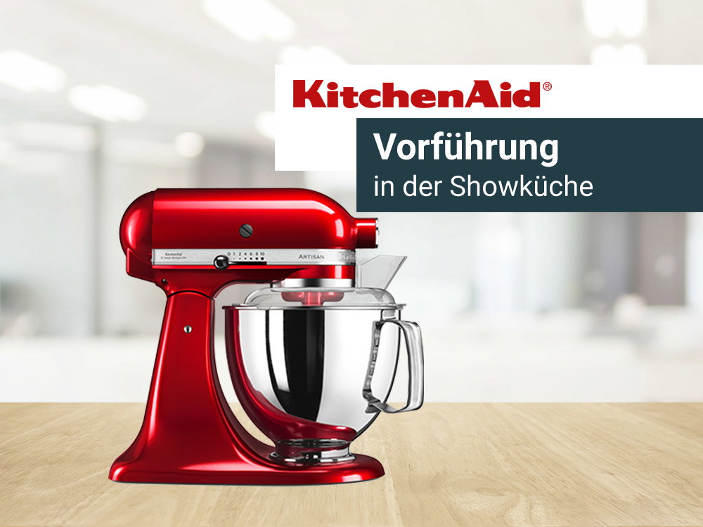Roter Standmixer von KitchenAid auf einer hölzernen Arbeitsplatte, mit Werbetext für eine Vorführung in der Showküche.