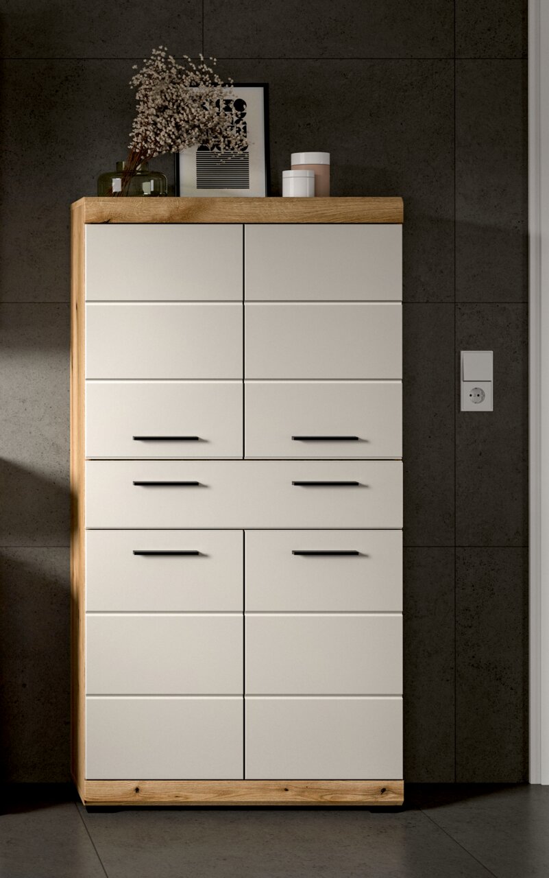 Moderne Kommode mit hellgrauen Fronten, Eichenholzrahmen und schwarzen Griffen, frontal aus leicht erhöhter Perspektive fotografiert, dekoriert mit Vase, Bild und Dosen auf der Holzplatte vor grauer Wand.