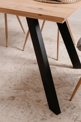 Nahaufnahme eines Esstisches mit schwarzem Metallbein und Holzplatte, seitliche Perspektive.