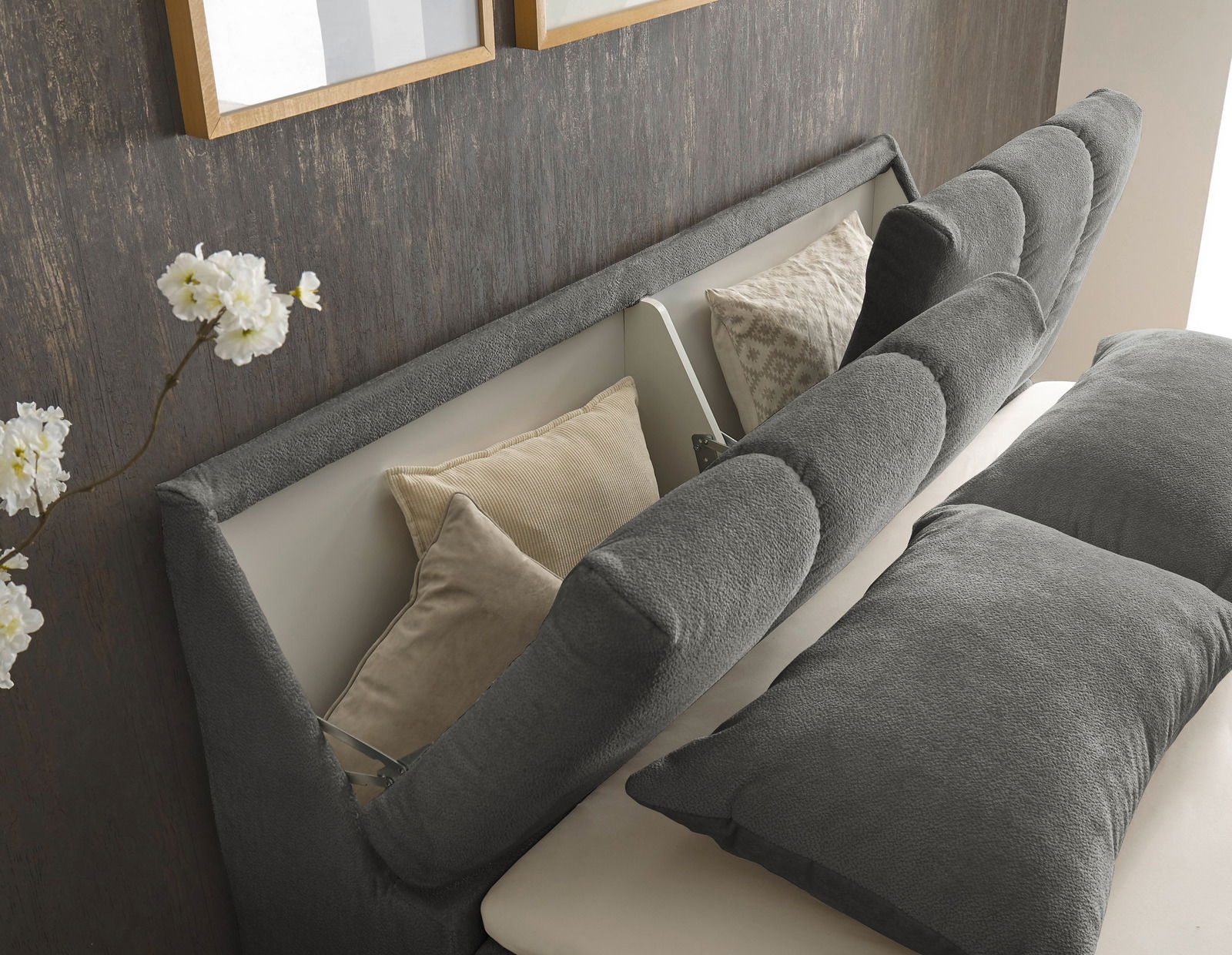 Nahaufnahme eines Boxspringbetts mit grauem Kopfteil und Kissen, seitliche Perspektive