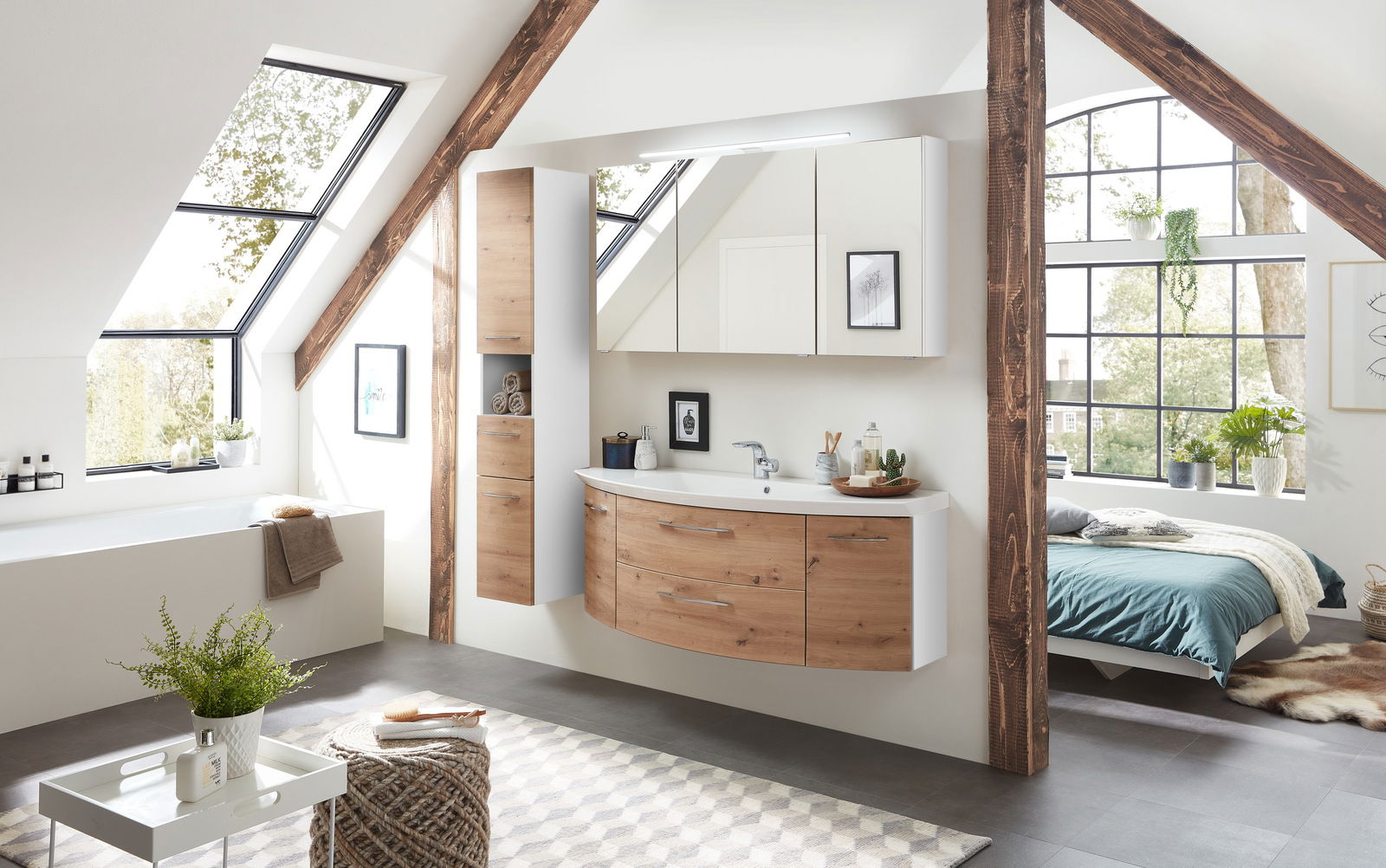 Sadena Badkombination 3-tlg. PLAKA Moderne Badkombination in einem hellen Dachgeschosszimmer mit großen Fenstern. Die Kombination besteht aus einem hängenden Waschtisch mit Holzfronten und einem großen Spiegel. Perspektive: Frontalansicht.