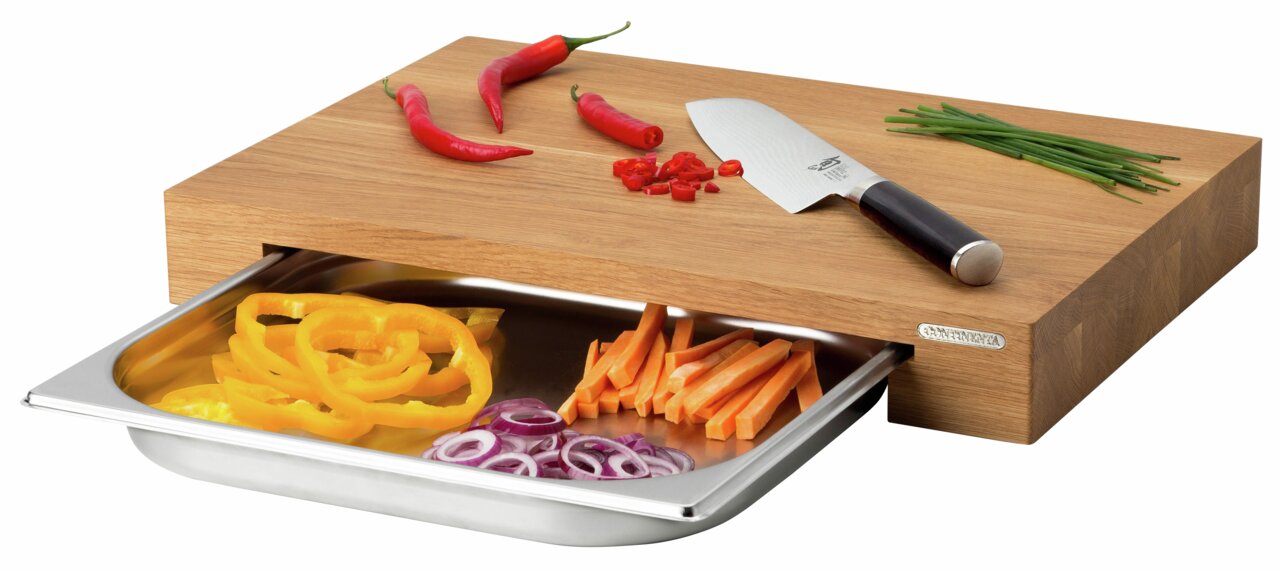 Multifunktionsbrett mit Schublade, darauf liegen rote Chilischoten, ein Messer und Schnittlauch. Die Schublade ist mit geschnittenem Gemüse gefüllt. Perspektive von schräg oben.
