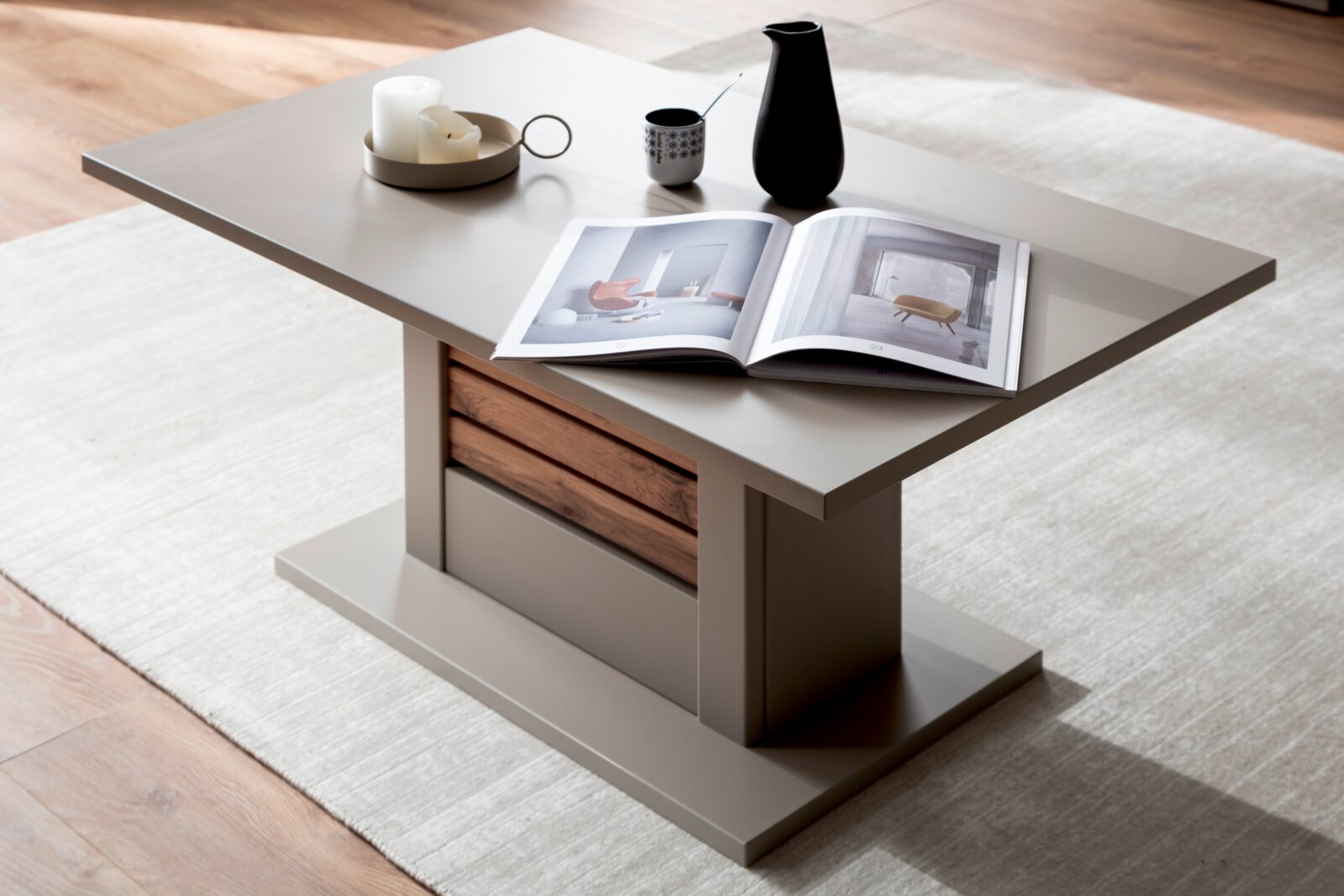 Zurbrüggen Salontafel LÜTTICH Moderner Couchtisch in Taupe mit Holz-Akzent und breitem Sockel, dekoriert mit offenem Magazin und Keramikvase, fotografiert aus schräger Perspektive von oben (3/4-Ansicht) im Wohnzimmer auf hellem Teppich.