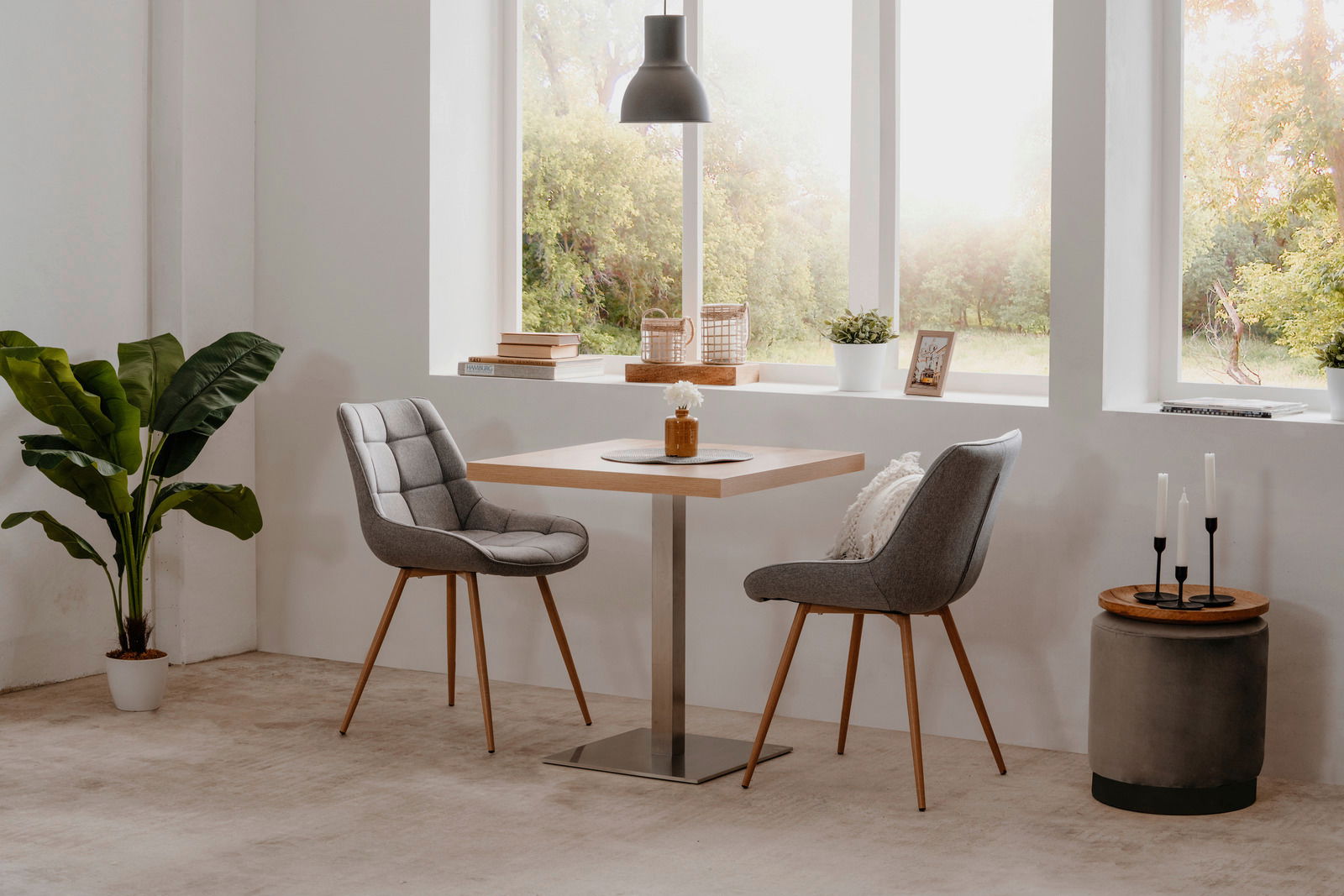 Moderner Esstisch QUADRATO mit quadratischer Holzplatte und Metallfuß, umgeben von zwei gepolsterten Stühlen in einem hellen Raum mit großen Fenstern, seitliche Perspektive.