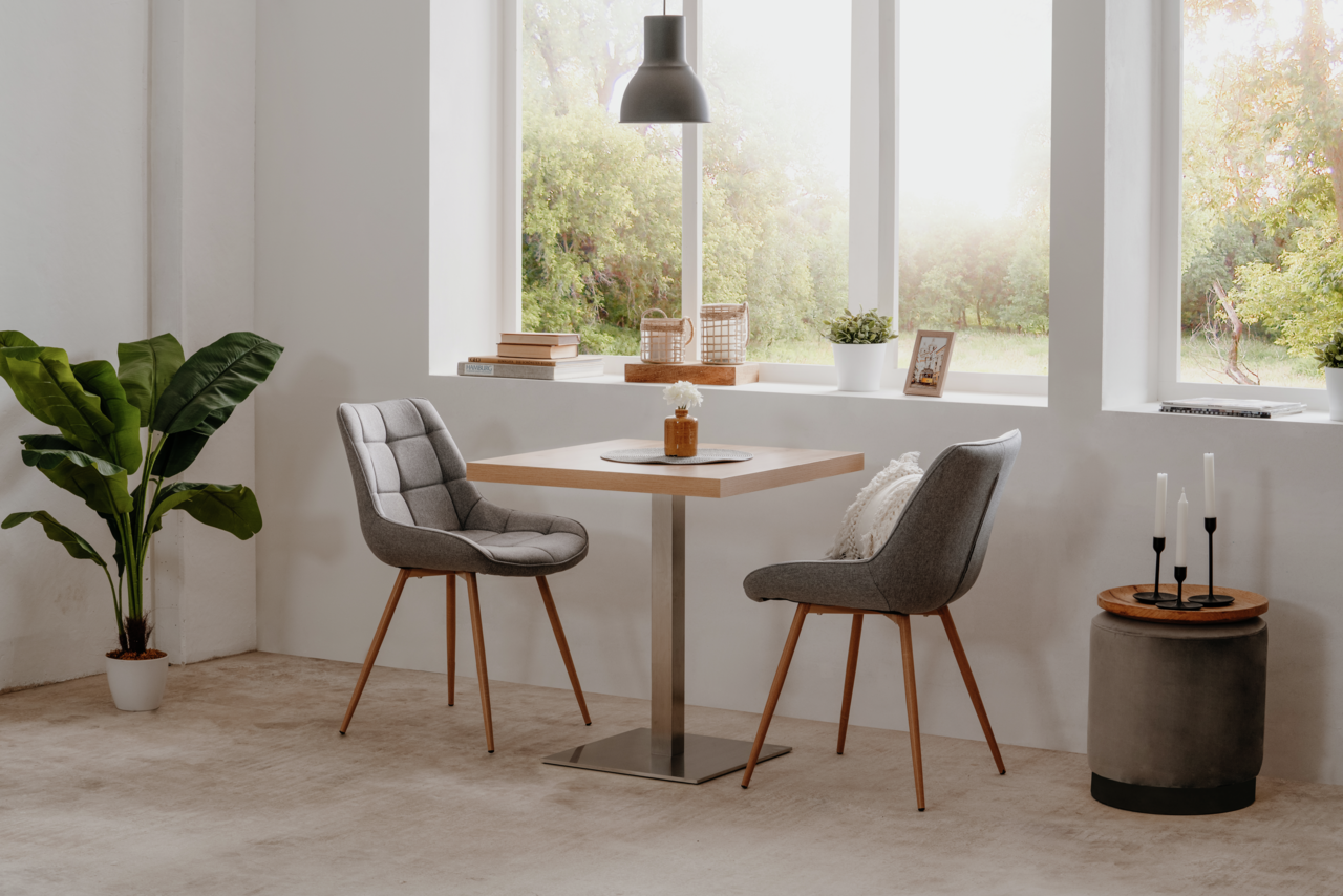 Moderner Esstisch QUADRATO mit quadratischer Holzplatte und Metallfuß, umgeben von zwei gepolsterten Stühlen in einem hellen Raum mit großen Fenstern, seitliche Perspektive.