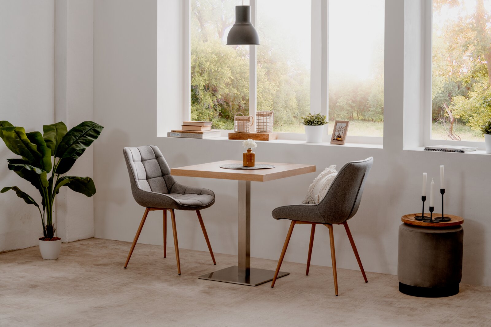 Moderner Esstisch QUADRATO mit quadratischer Holzplatte und Metallfuß, umgeben von zwei gepolsterten Stühlen in einem hellen Raum mit großen Fenstern, seitliche Perspektive.