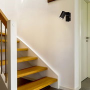 Schwarzer LED-Spot ISIL A an der Wand montiert, seitliche Perspektive, beleuchtet eine Treppe in einem modernen Innenraum.