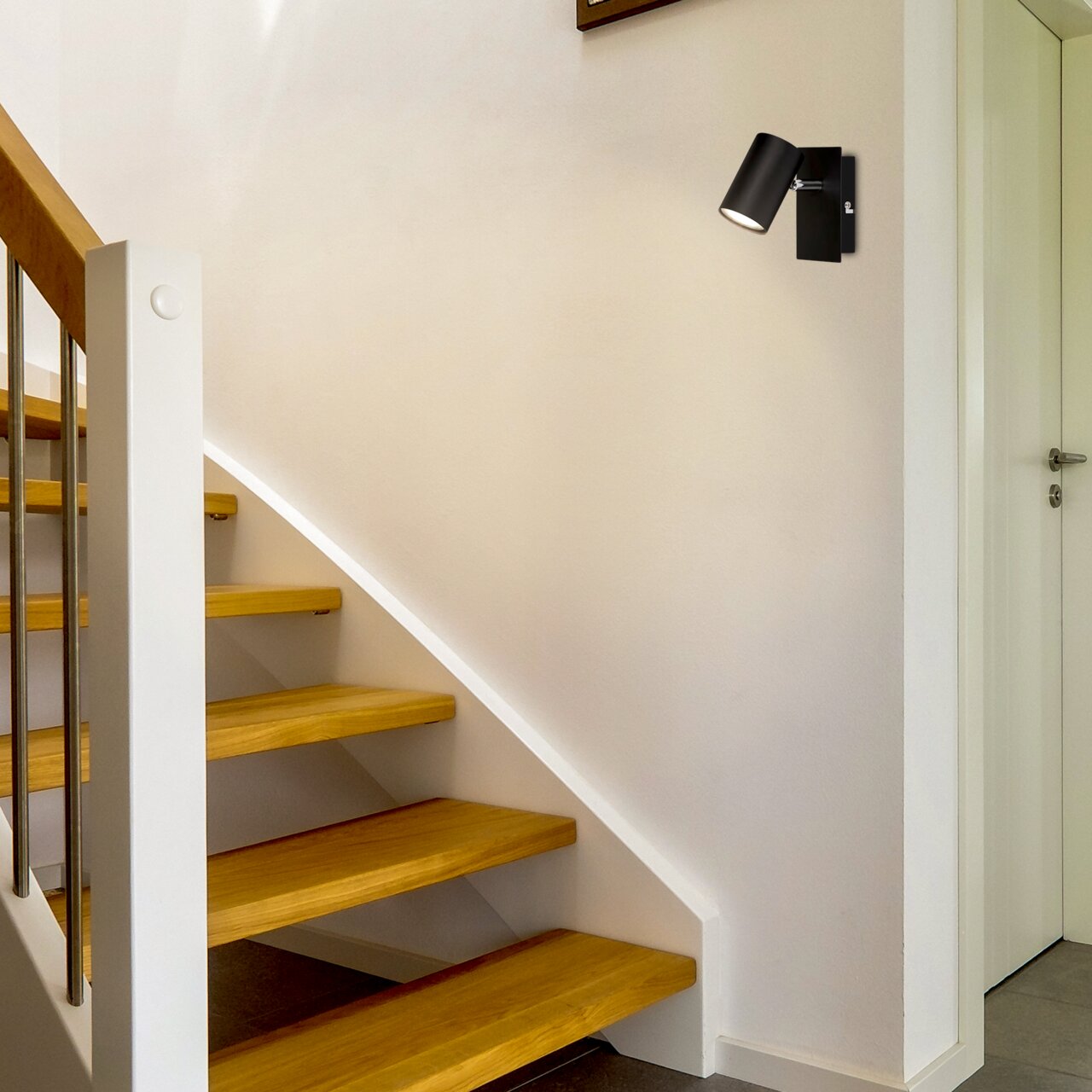 Schwarzer LED-Spot ISIL A an der Wand montiert, seitliche Perspektive, beleuchtet eine Treppe in einem modernen Innenraum.