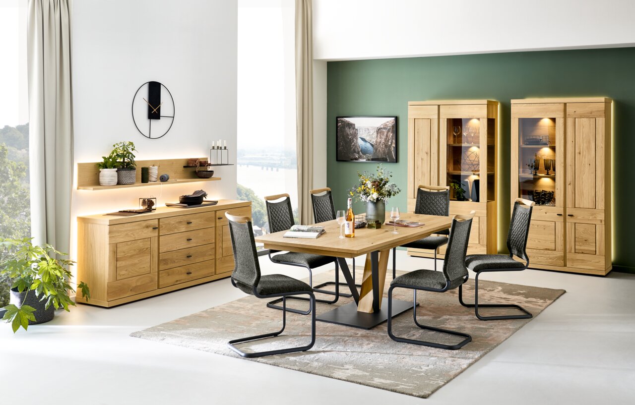Eetkamer met een moderne houten tafel, zes stoelen, een dressoir en twee verlichte vitrinekasten, zijaanzicht