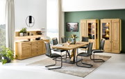 Eetkamer met een moderne houten tafel, zes stoelen, een dressoir en twee verlichte vitrinekasten, zijaanzicht