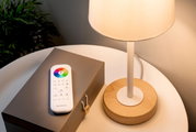 Afstandsbediening met kleurencirkel en knoppen op een tafel naast een lamp, gezien van bovenaf