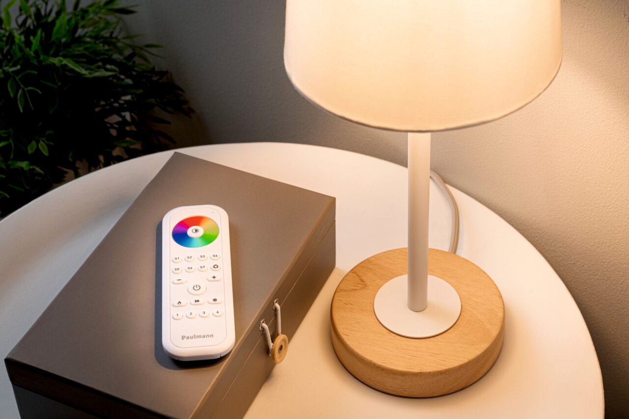 Fernbedienung mit Farbkreis und Tasten auf einem Tisch neben einer Lampe, von oben betrachtet