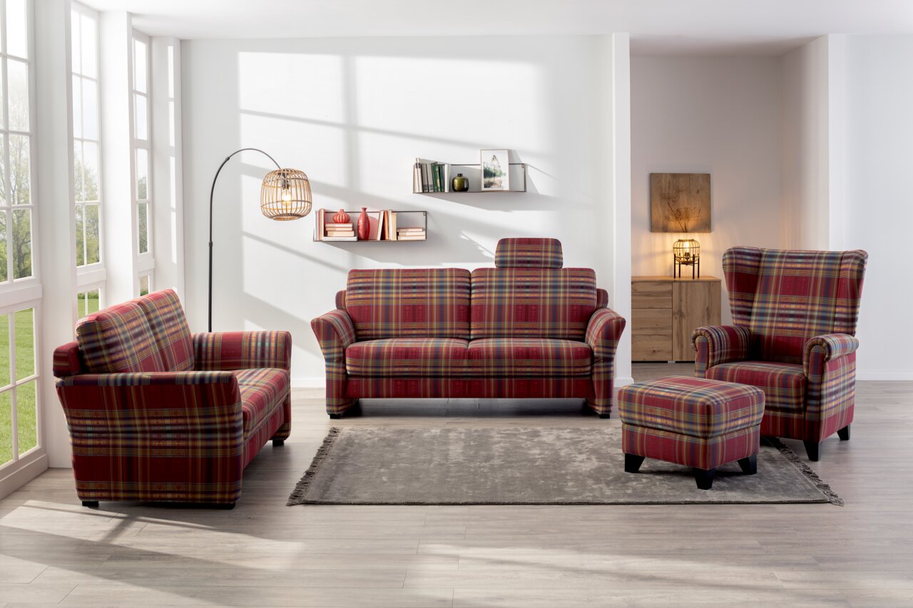 Wohnzimmer mit kariertem Sofa-Set bestehend aus einem 3er-Sofa, einem 2er-Sofa, einem Ohrensessel und einem Hocker, aus der Frontalperspektive fotografiert.