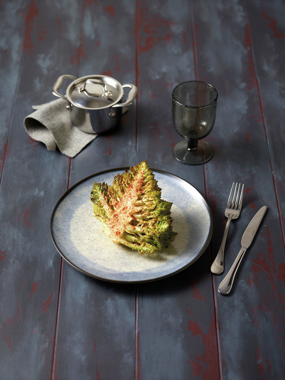 Vogelperspektive auf einen gedeckten Tisch mit einem Teller aus dem Tellerset Shade Matt Sea, darauf ein Stück Romanesco, daneben Besteck, ein Glas und ein kleiner Topf.