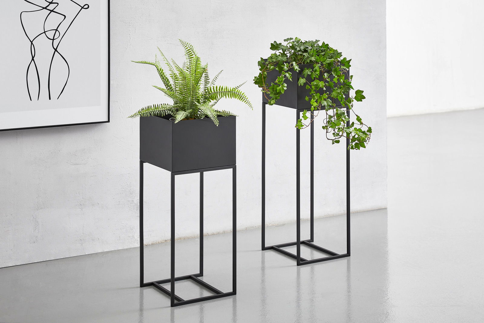 Zwei moderne Blumensäulen aus schwarzem Metall mit Pflanzen, fotografiert aus einer frontalen Perspektive.