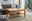 Holz-Couchtisch mit Ablage, umgeben von einem modernen Wohnzimmer mit grauem Sofa und Pflanzen, seitliche Perspektive