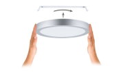 Runde LED-Deckenleuchte in Silber/Weiß wird von zwei Händen gehalten; Montagebügel darüber mit Pfeilen zur Drehmontage, Ansicht leicht von unten in Frontperspektive.