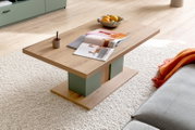 Moderner Couchtisch aus Holz mit grünen Akzenten, von schräg oben fotografiert. Auf dem Tisch liegen Zeitschriften, eine Tasse und eine Schale mit Obst.