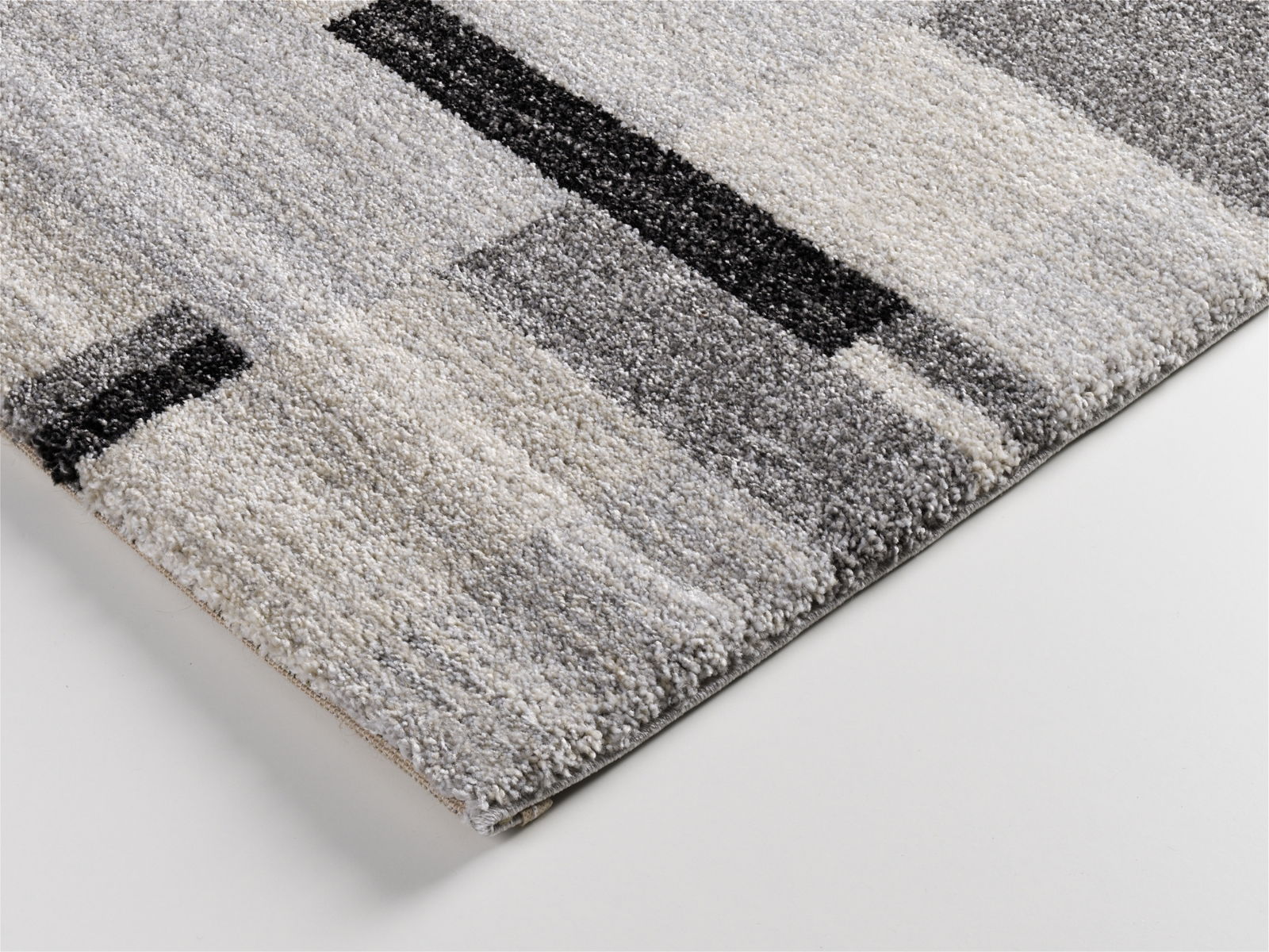 Nahaufnahme eines modernen Teppichs mit geometrischem Muster in Grautönen, perspektivisch von der Seite aufgenommen.