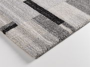 Nahaufnahme eines modernen Teppichs mit geometrischem Muster in Grautönen, perspektivisch von der Seite aufgenommen.