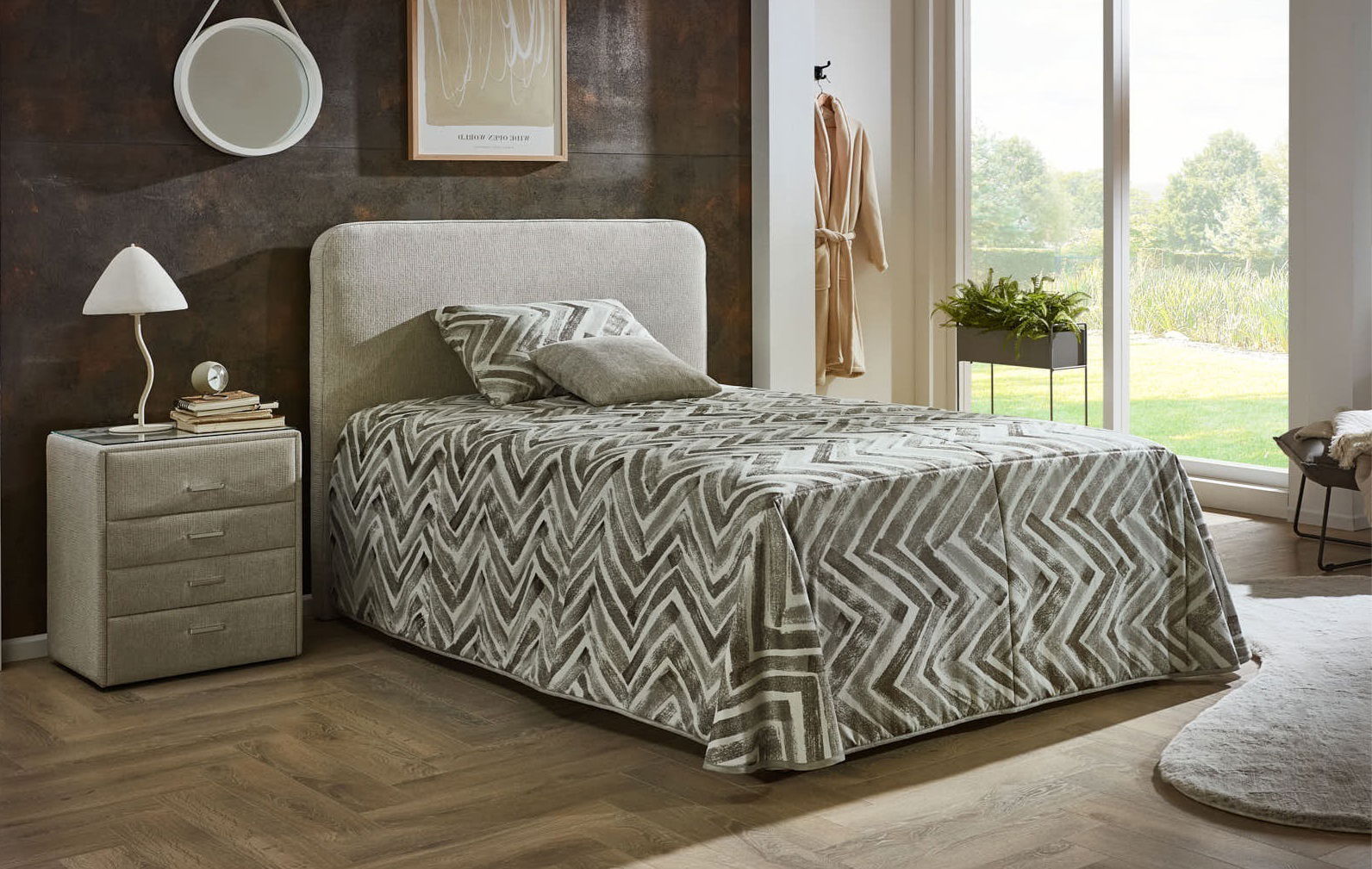 Gemütliches Polsterbett in einem modernen Schlafzimmer, seitliche Perspektive, mit grauem Zickzack-Muster auf der Bettdecke und passendem Nachttisch.