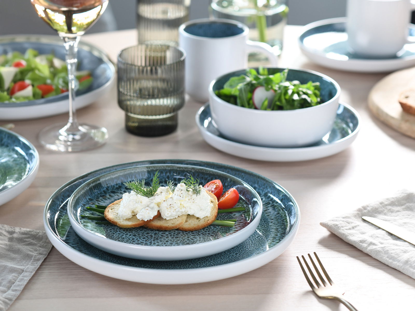 Kombiservice 16-tlg. Eisblau, bestehend aus Tellern und Schalen in einem eleganten Design, auf einem gedeckten Tisch von oben fotografiert.