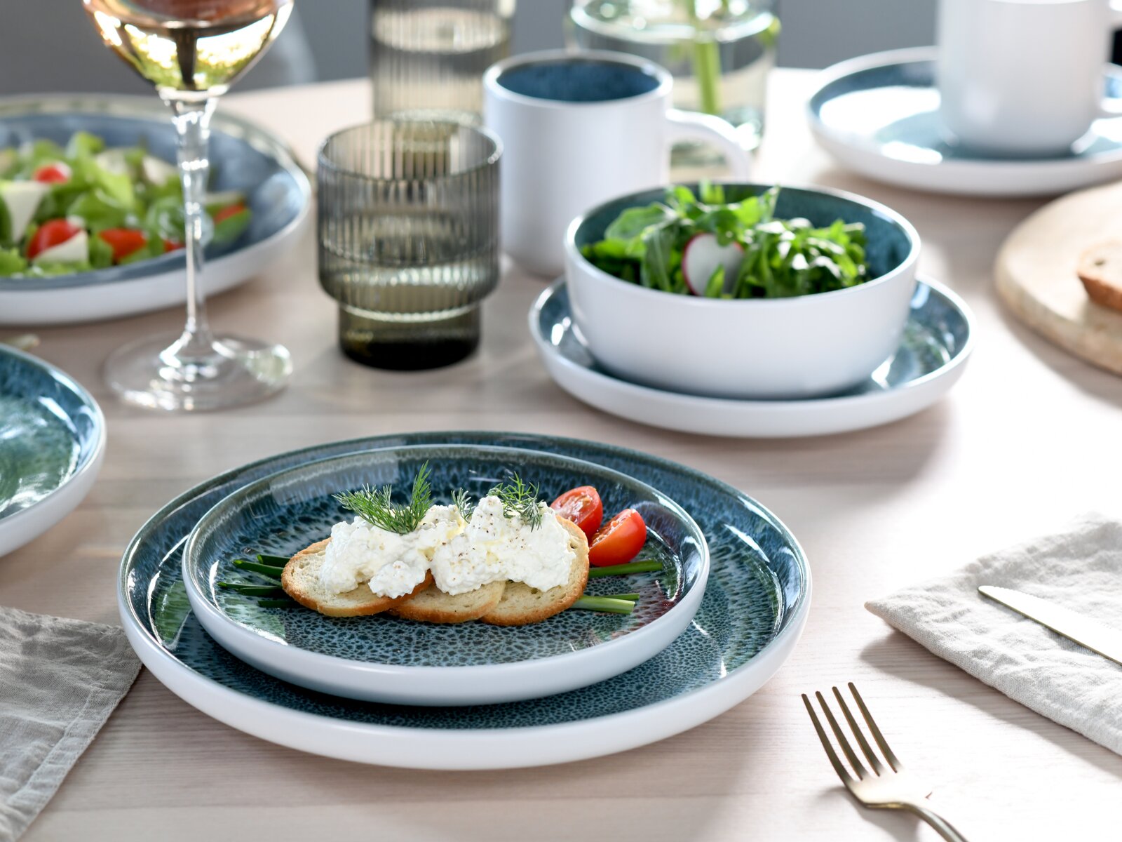 Serviesset van 16-delig, ijsblauw, bestaande uit borden en schalen in een elegant ontwerp, gefotografeerd van bovenaf op een gedekte tafel.