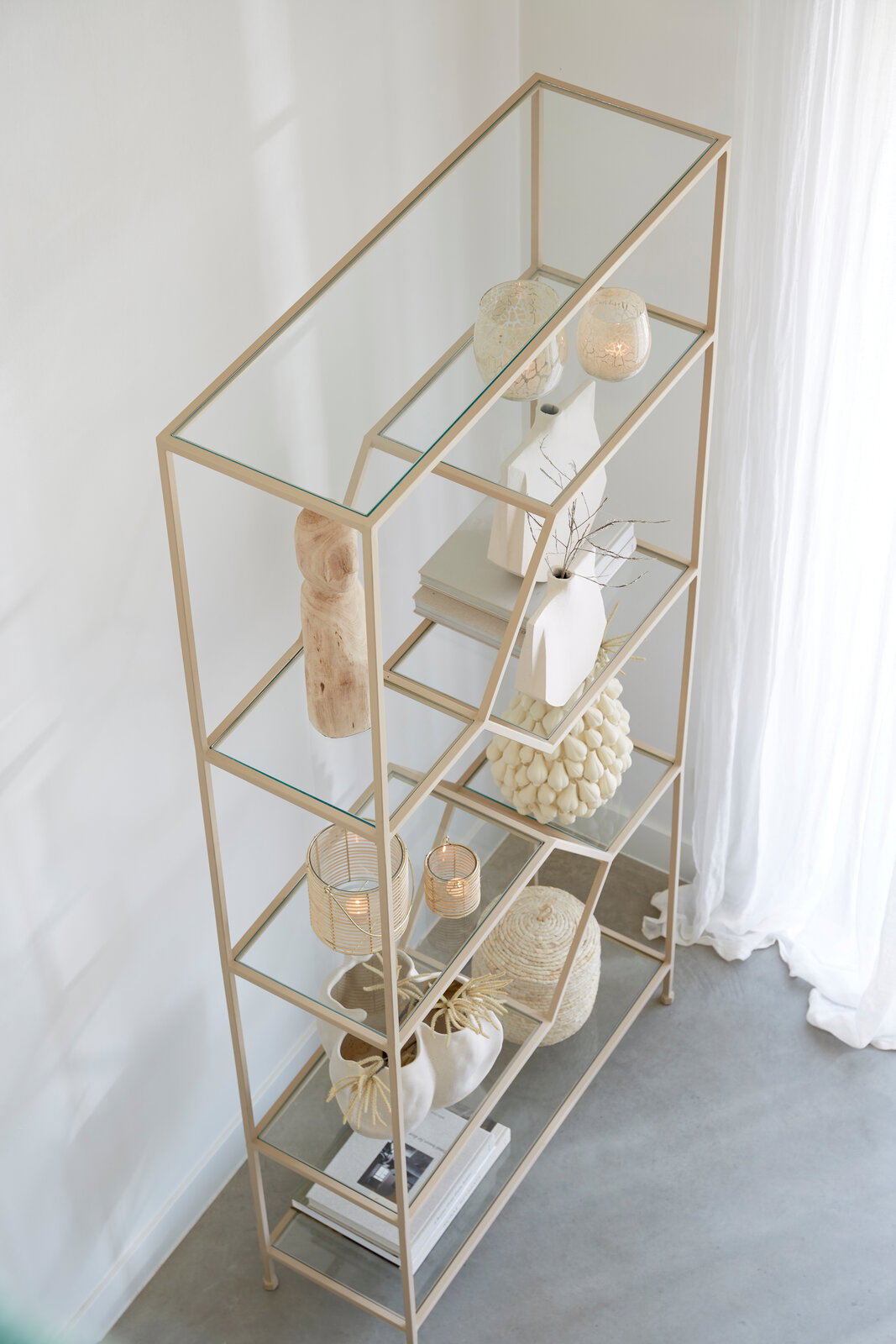 Modernes Standregal aus Metall mit Glasböden, dekoriert mit Vasen und Büchern, aus der Vogelperspektive fotografiert.