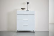 Weiße Schubkastenkommode mit vier Schubladen, dekoriert mit einer Lampe und einer Schale, aus frontaler Perspektive fotografiert.