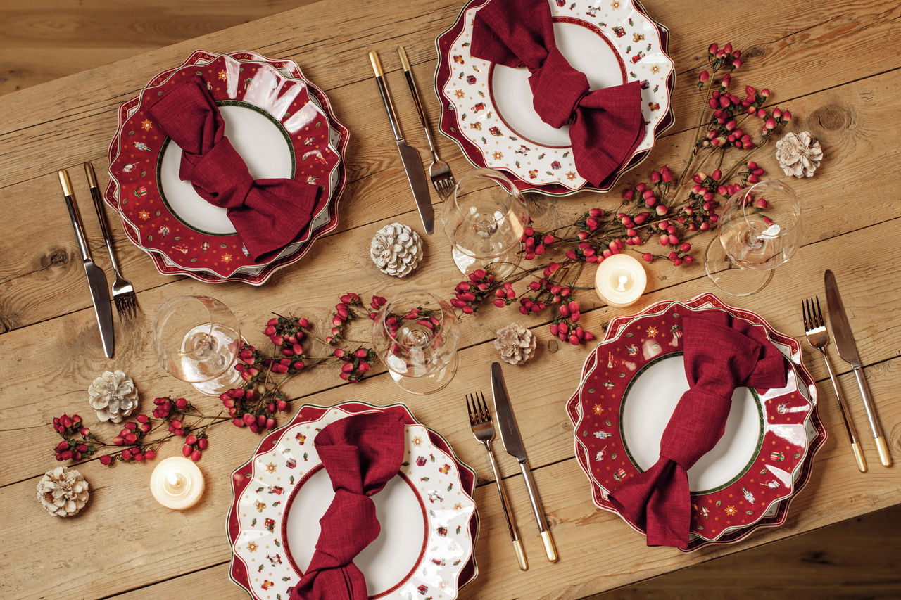 Vogelperspektive auf einen festlich gedeckten Tisch mit roten Suppentellern aus der Serie Toy's Delight, dekoriert mit roten Servietten, Tannenzapfen und Kerzen.