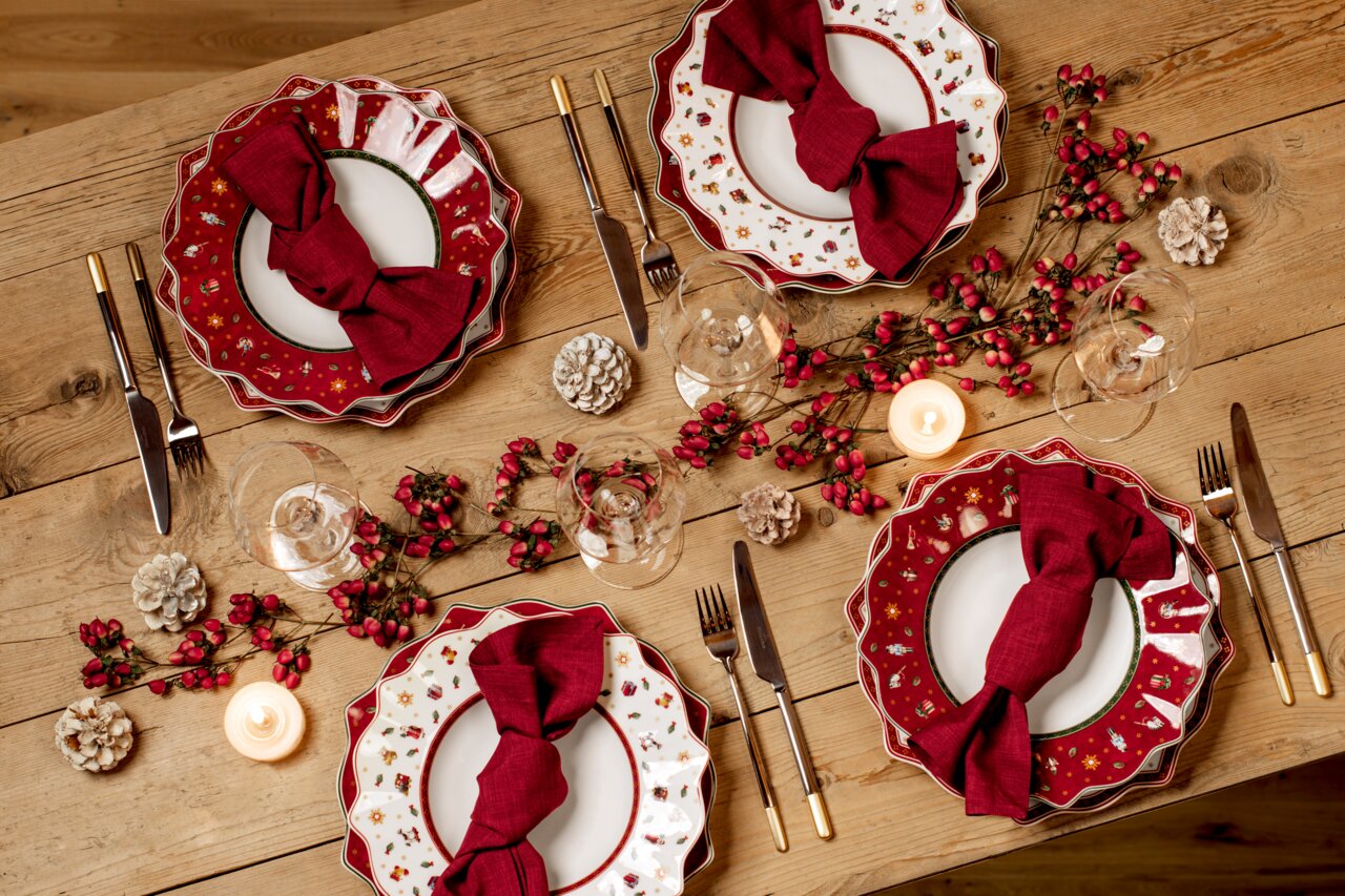 Vogelperspektive auf einen festlich gedeckten Tisch mit roten Suppentellern aus der Serie Toy's Delight, dekoriert mit roten Servietten, Tannenzapfen und Kerzen.
