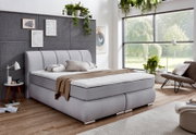 Modernes Boxspringbett in einem stilvollen Schlafzimmer mit grauem Kopfteil, dekorativen Kissen und Tagesdecke, seitliche Perspektive.