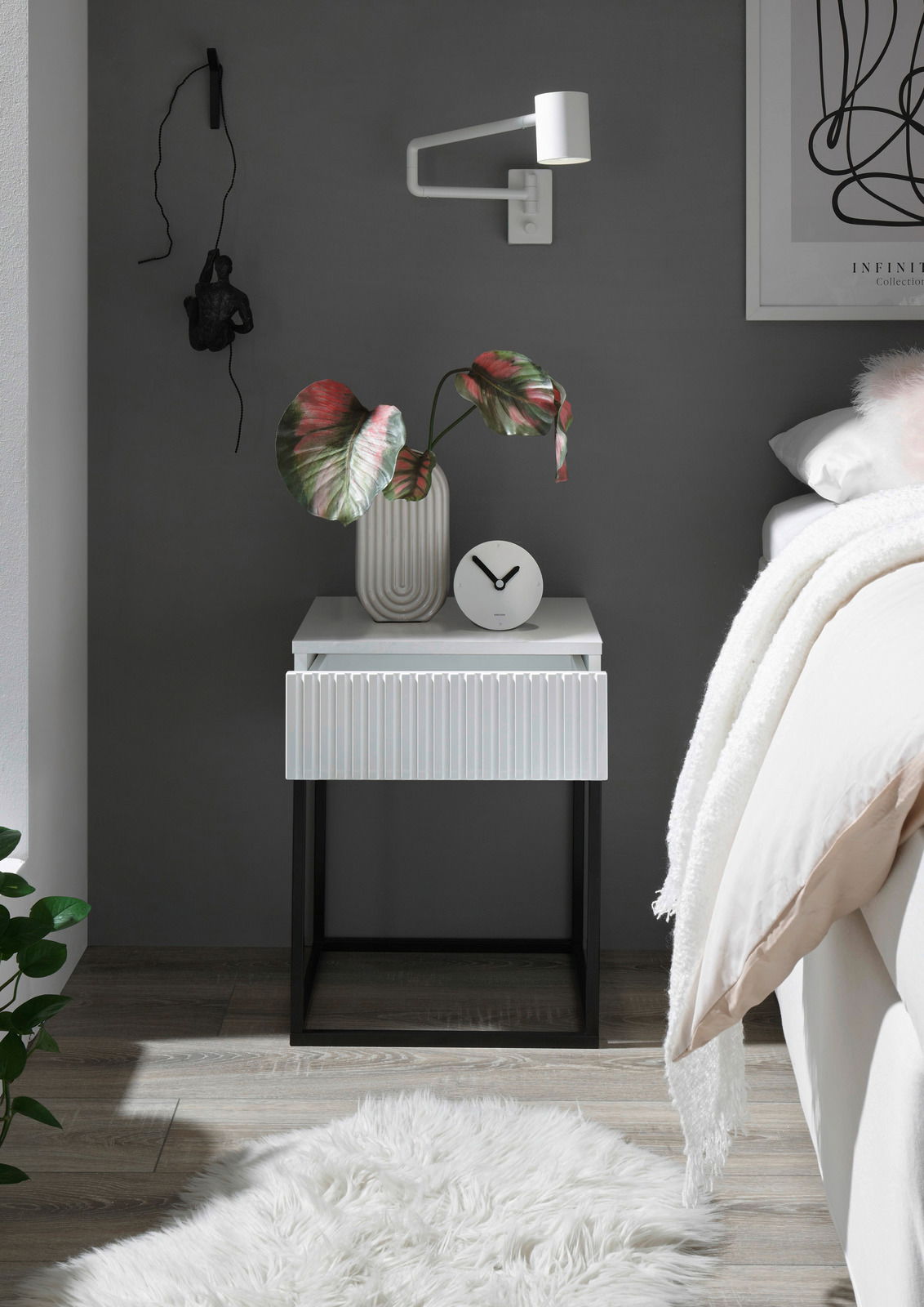 Moderne Nachtkommode mit weißer Oberfläche und geriffelter Schublade, dekoriert mit einer Vase und einer Uhr, aus frontaler Perspektive.