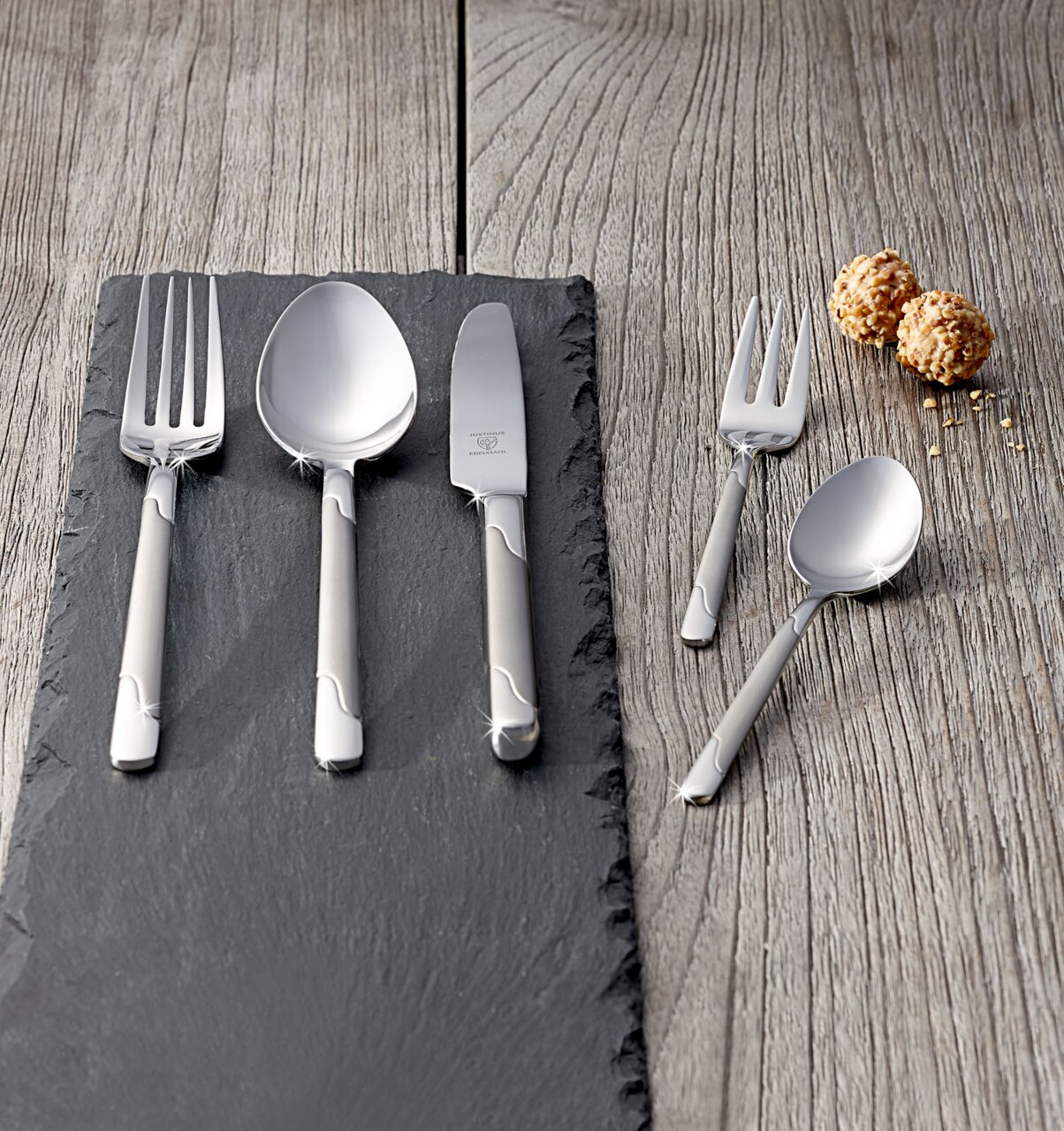 Justinus Besteck Viva 60-tlg. Elegantes Besteckset Viva 60-tlg. aus Edelstahl, bestehend aus Gabel, Löffel, Messer und Dessertbesteck, auf einer Schieferplatte präsentiert, mit einer modernen und stilvollen Optik. Perspektive von oben.