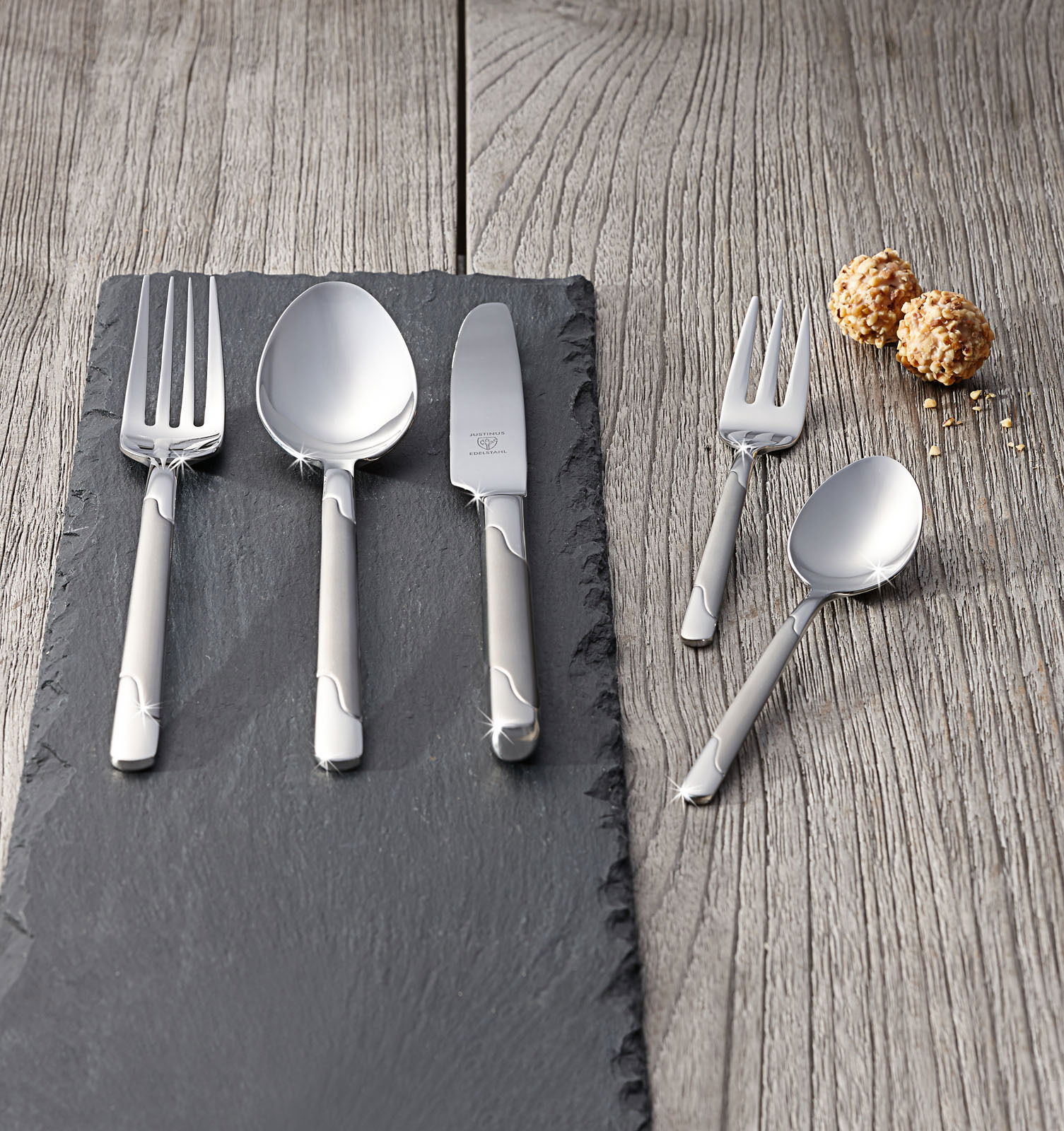 Justinus Besteck Viva 60-tlg. Elegantes Besteckset Viva 60-tlg. aus Edelstahl, bestehend aus Gabel, Löffel, Messer und Dessertbesteck, auf einer Schieferplatte präsentiert, mit einer modernen und stilvollen Optik. Perspektive von oben.