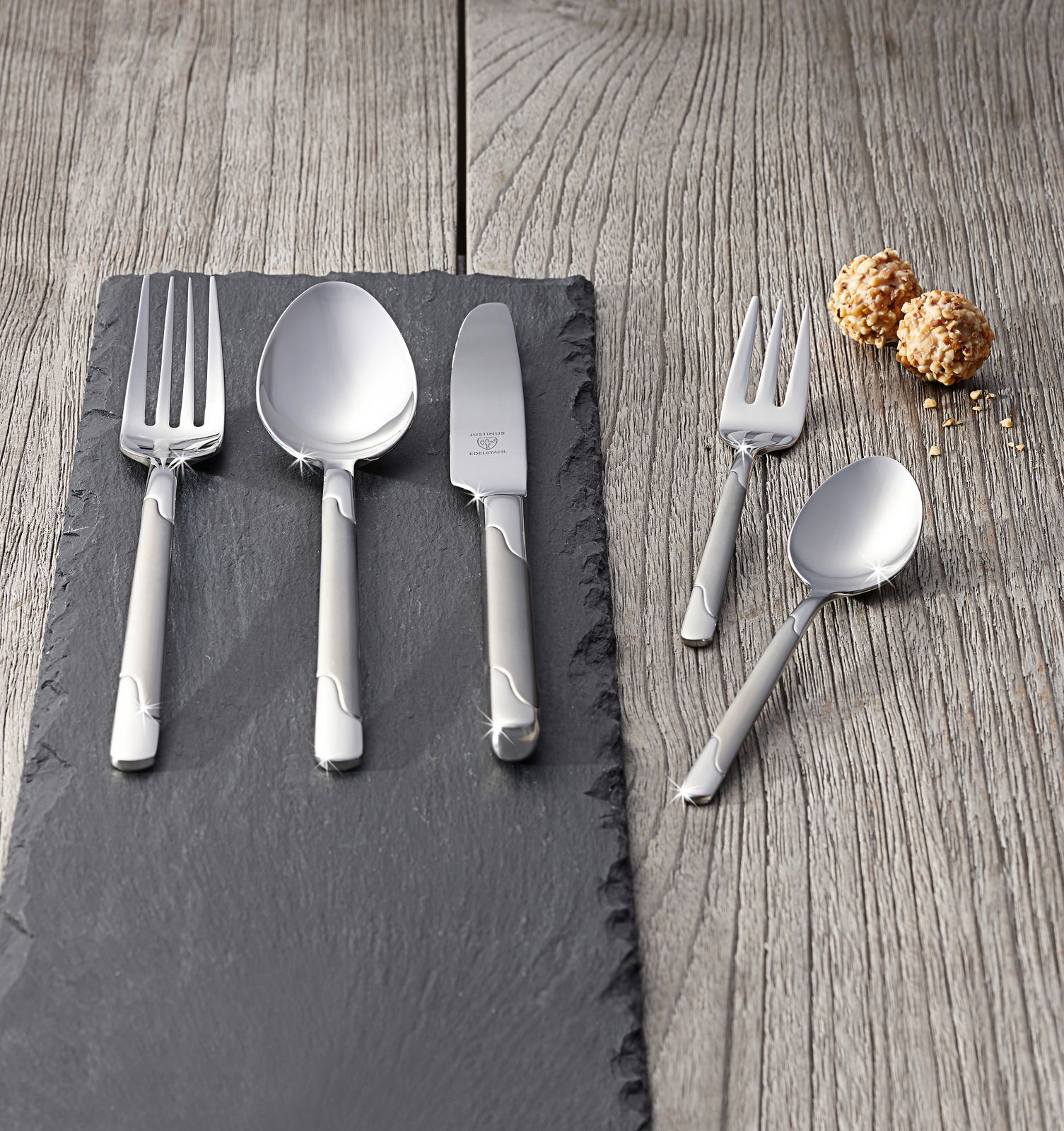 Elegantes Besteckset Viva 60-tlg. aus Edelstahl, bestehend aus Gabel, Löffel, Messer und Dessertbesteck, auf einer Schieferplatte präsentiert, mit einer modernen und stilvollen Optik. Perspektive von oben.