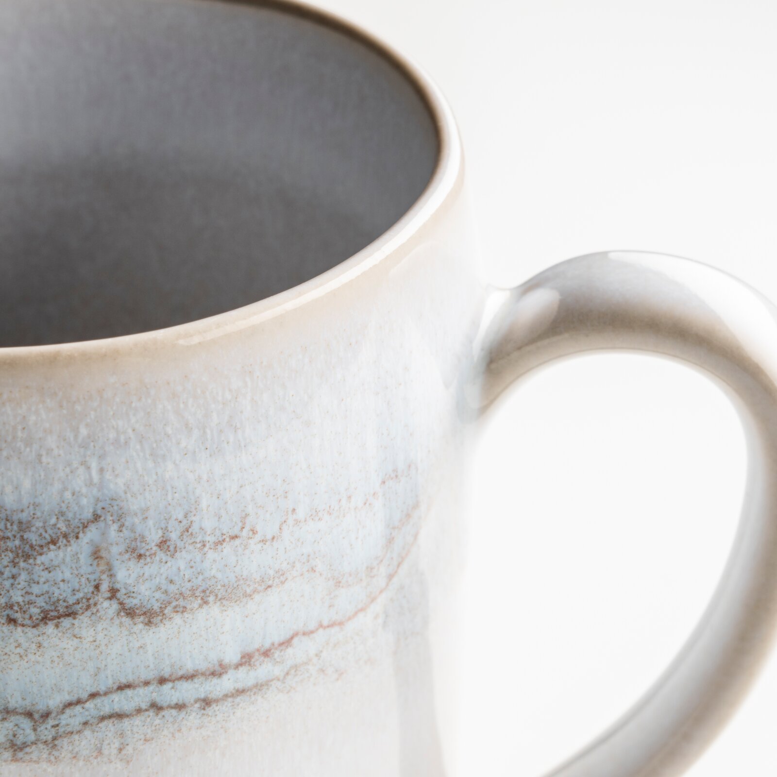 Gipfelstück Kaffeebecher 4er-Set TIEFER SEE Detailaufnahme einer glasierten Keramik-Kaffeetasse in Weiß mit blau-brauner Sprenkel-Optik und Henkel, Perspektive: Nahaufnahme schräg von oben vor weißem Hintergrund