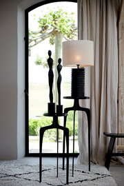 Moderner Lampenschirm auf einem eleganten schwarzen Ständer, im Vordergrund mit Blick auf ein Fenster mit Garten im Hintergrund.