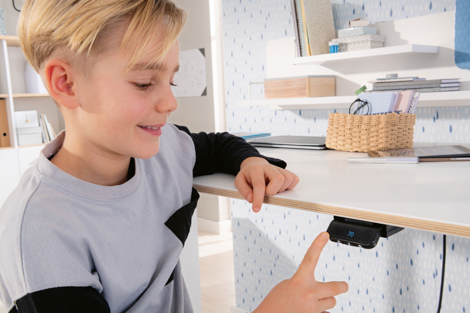 Junge bedient einen höhenverstellbaren Schreibtisch mit digitalem Display, seitliche Perspektive