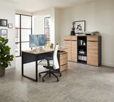 Moderner Schreibtisch mit Holzoberfläche und schwarzem Metallgestell, seitliche Perspektive. Im Hintergrund ein Aktenschrank mit Regalen und Dekorationen.