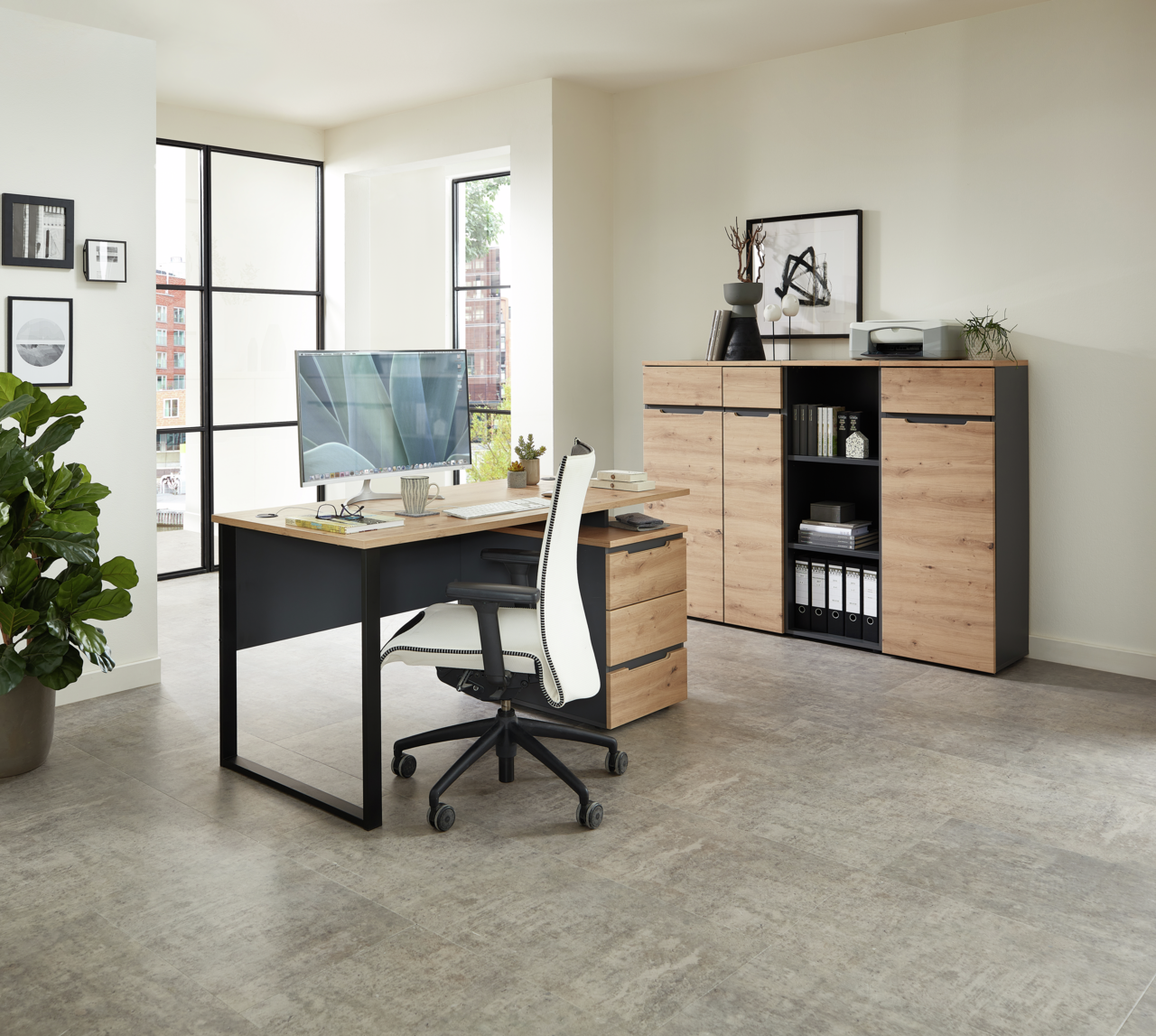 Voleo Schreibtisch DETROIT Moderner Schreibtisch mit Holzoberfläche und schwarzem Metallgestell, seitliche Perspektive. Im Hintergrund ein Aktenschrank mit Regalen und Dekorationen.