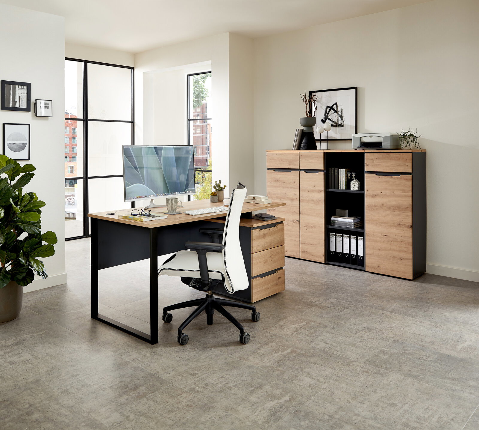 Moderner Schreibtisch mit Holzoberfläche und schwarzem Metallgestell, seitliche Perspektive. Im Hintergrund ein Aktenschrank mit Regalen und Dekorationen.