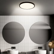 Moderne ronde plafondlamp met zwarte rand en warme lichtdiffusor in een badkamer boven twee ronde spiegels en dubbele wastafels, gezien van onderaf/laag standpunt richting plafond.
