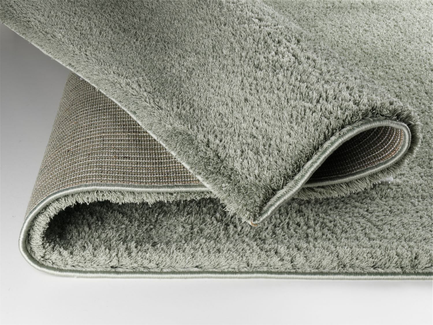 Nahaufnahme eines gefalteten, weichen, grauen Teppichs mit flauschiger Oberfläche und rutschfester Unterseite.