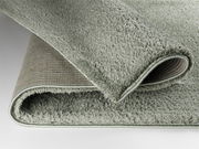 Nahaufnahme eines gefalteten, weichen, grauen Teppichs mit flauschiger Oberfläche und rutschfester Unterseite.