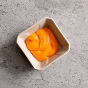 Quadratische, cremefarbene Keramikschale mit glänzendem orangefarbenem Püree auf grauer Steinoberfläche, aufgenommen aus der Vogelperspektive (Top-Down).