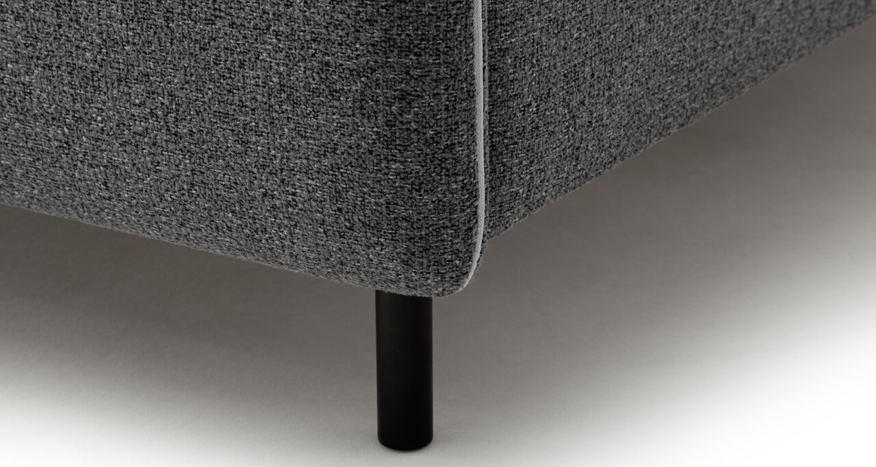 Nahaufnahme einer Ecke eines grauen Polsterbetts mit schwarzem Bein, seitliche Perspektive