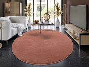 Runder, roter Uni-Teppich in einem modernen Wohnzimmer mit Blick auf eine gemütliche Sitzecke und einen Fernseher.