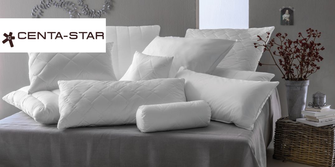 Een groot aantal witte kussens in verschillende vormen en maten op een bed. Het Centa-Star-logo in de hoek.