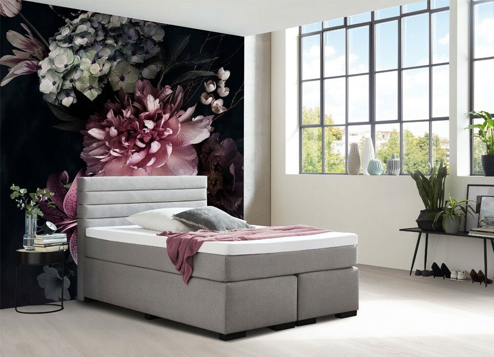 Graues Boxspringbett in modernem Schlafzimmer mit großen Fenstern und floralem Wandbild, seitliche Perspektive